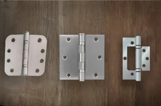 Three stainless steel hinges displayed on a wooden surface, showcasing high-quality hardware options offered by hinges manufacturers in Hyderabad for domestic, commercial, and industrial applications.