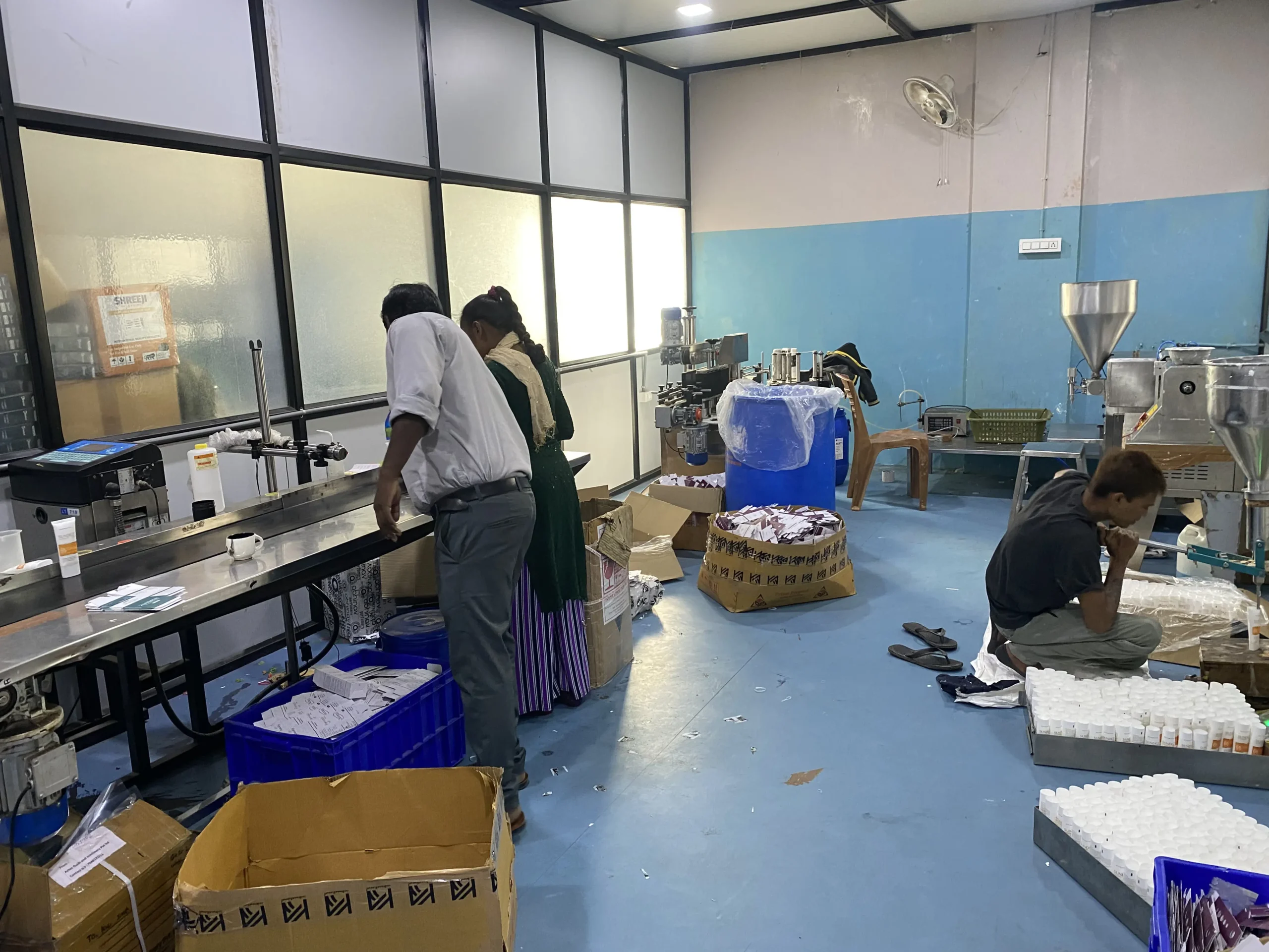 Workers assembling and packaging derma skin care products at the KA International manufacturing facility in India, featuring industrial equipment and packaging materials, showcasing the production process of high-quality derma products.