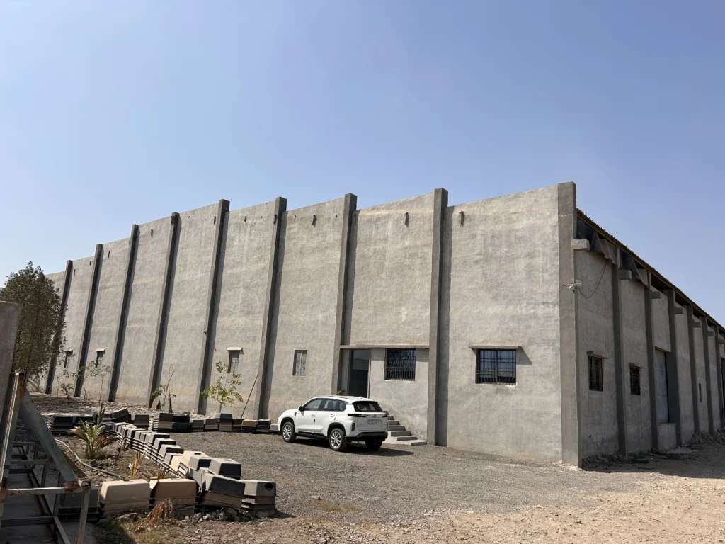 Front view of Dinora's quartz kitchen sink manufacturing unit featuring a large concrete industrial building under clear blue sky