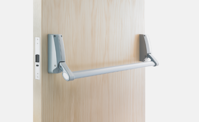 Silver fire escape door handle bar on wooden emergency exit door, ergonomically designed for single-motion panic operation and fire-rated safety compliance