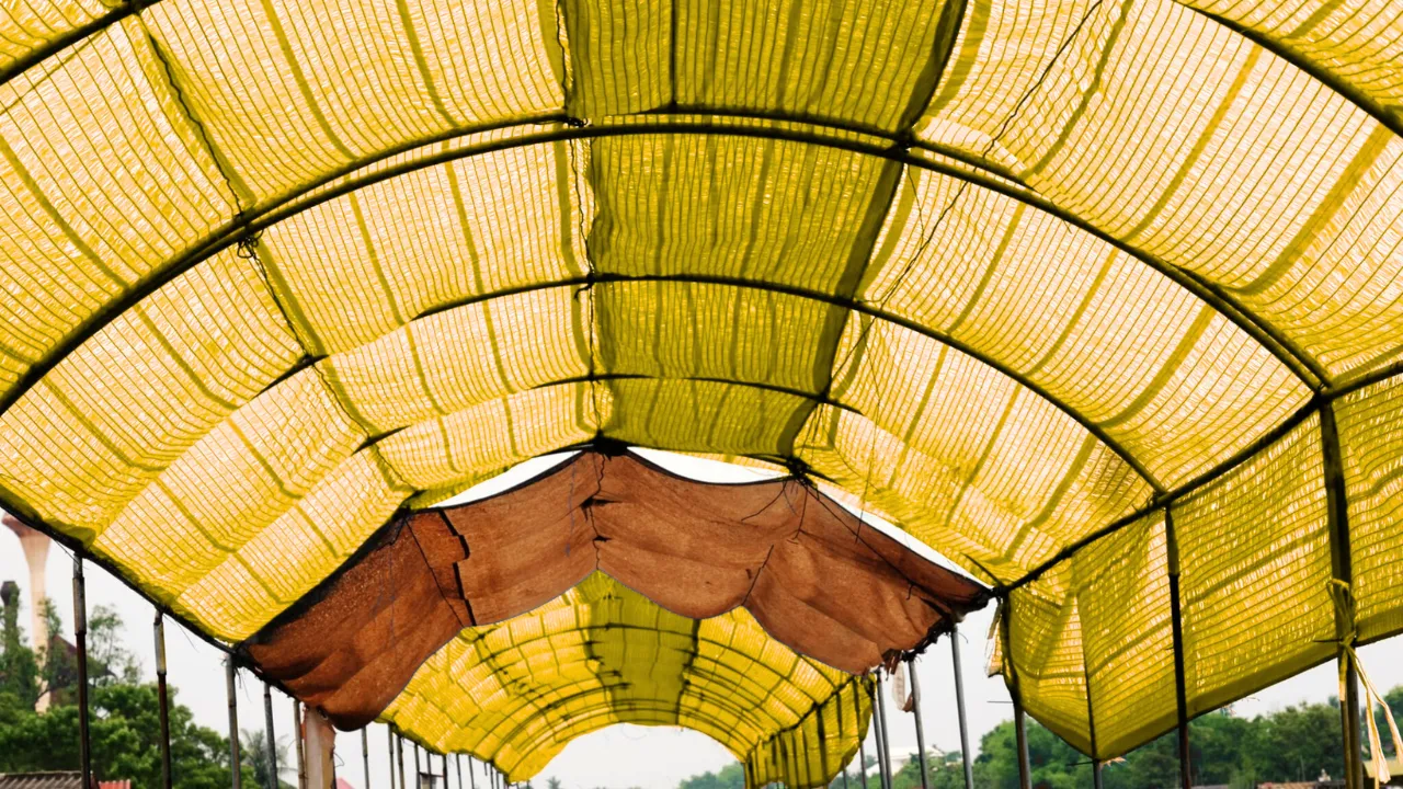 Yellow HDPE monsoon shed tarpaulin cover installed on a temporary structure, used for protecting goods and machinery at construction sites and warehouses during heavy rainfall, by top tarpaulin manufacturer in India