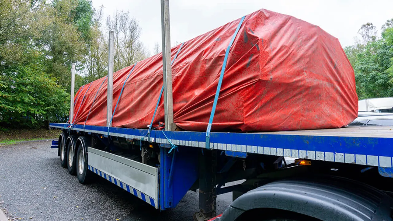 Flatbed trailer with red tarpaulin sheet securely covering cargo, showcasing waterproof truck tarpaulin from a leading tarpaulin manufacturer in India for transport and logistics use