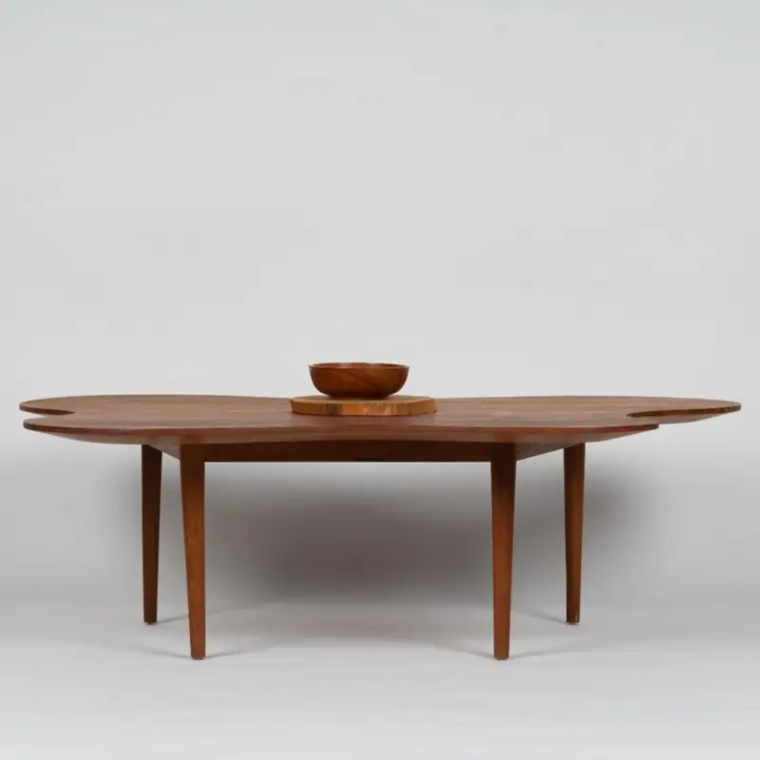 A distinctive reclaimed wood centre table featuring an organic, flowing design with rounded edges and sleek tapered legs. The table's unique shape adds a creative touch to the living room, complemented by a wooden bowl placed in the center. The rich wood finish highlights the natural beauty of reclaimed materials, making it a striking focal point in any modern space.