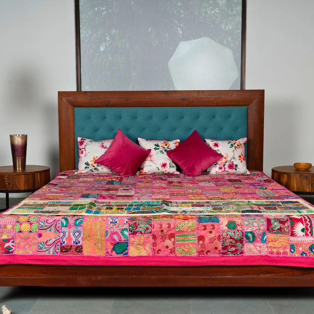 A beautifully crafted reclaimed wood bed featuring a solid wooden frame with a vibrant turquoise tufted headboard. The bed is adorned with a colorful patchwork quilt and plush pillows, adding warmth and personality to the space. The natural grain of the reclaimed wood complements the bold, decorative elements, creating a harmonious balance of rustic and modern design in the bedroom.