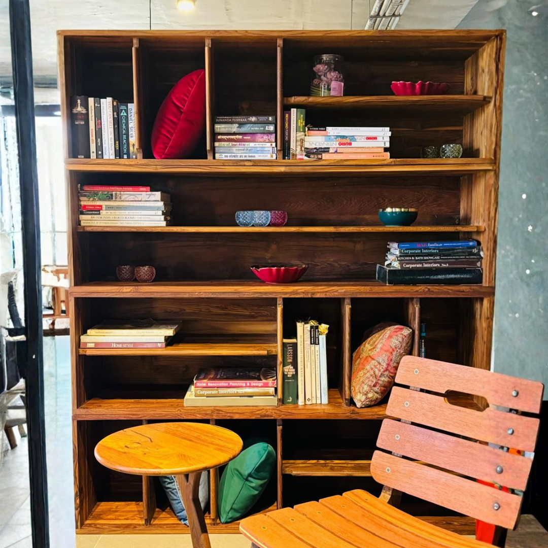 A reclaimed wood bookshelf with a clean, minimalist design, featuring open shelving that holds a mix of books, decorative bowls, and cushions. The natural wood finish adds warmth and texture to the space, while the well-organized design offers both functionality and visual appeal. Perfect for displaying books and decorative items, this piece combines practicality with the timeless charm of reclaimed wood. Ideal for living rooms, offices, or reading corners.