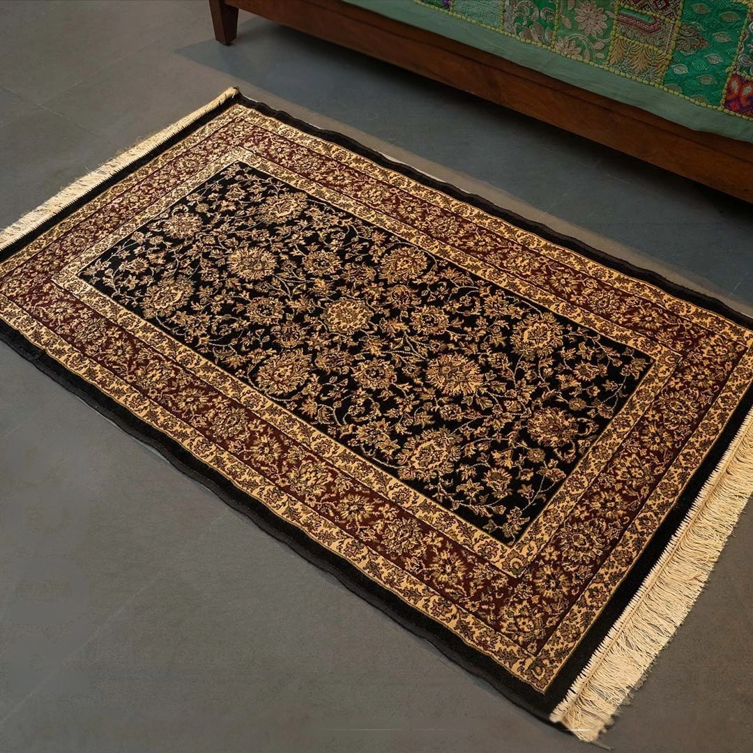 Kashmiri wool carpet with intricate floral patterns in dark tones placed on floor near sofa showcasing handmade craftsmanship and traditional rug design