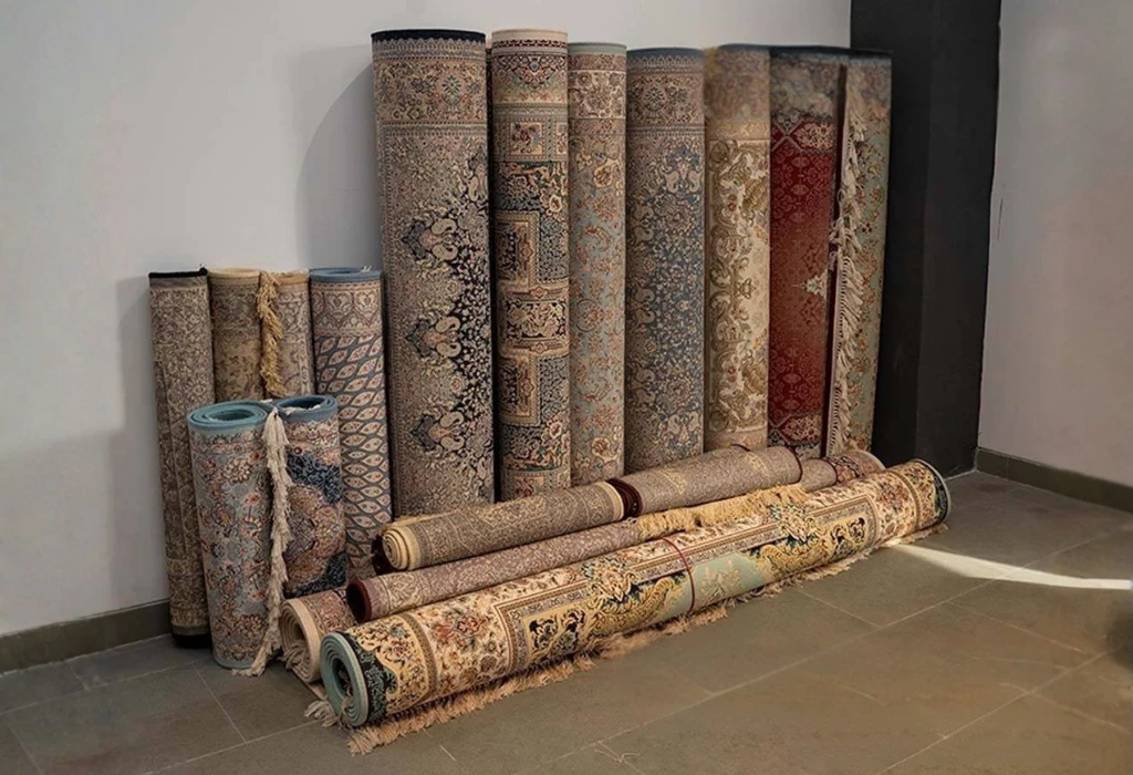 rolled premium Kashmiri carpets with intricate traditional patterns displayed against wall showcasing handwoven rug craftsmanship