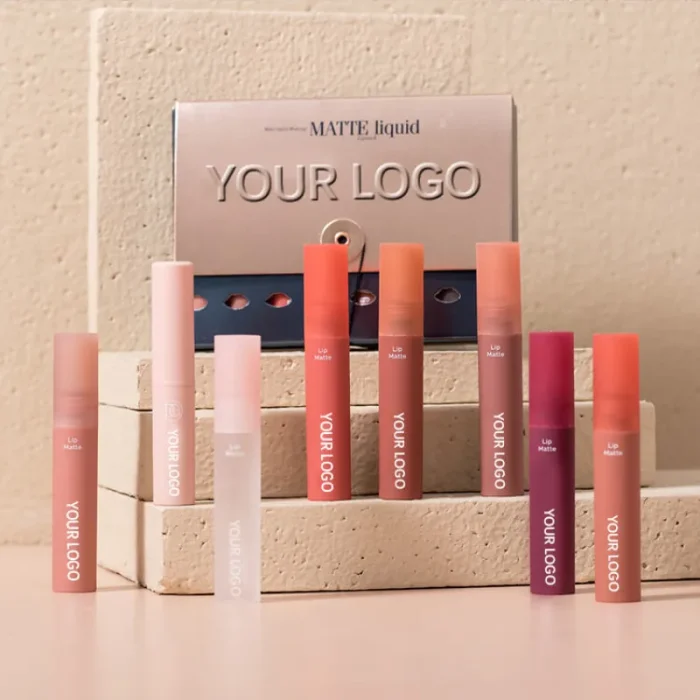 Display of various lip gloss tubes in different shades, showcasing a custom lip gloss line with "YOUR LOGO" branding, by a lip gloss private label manufacturers. The collection includes matte liquid lip gloss tubes in a range of pink, coral, and deep red hues.